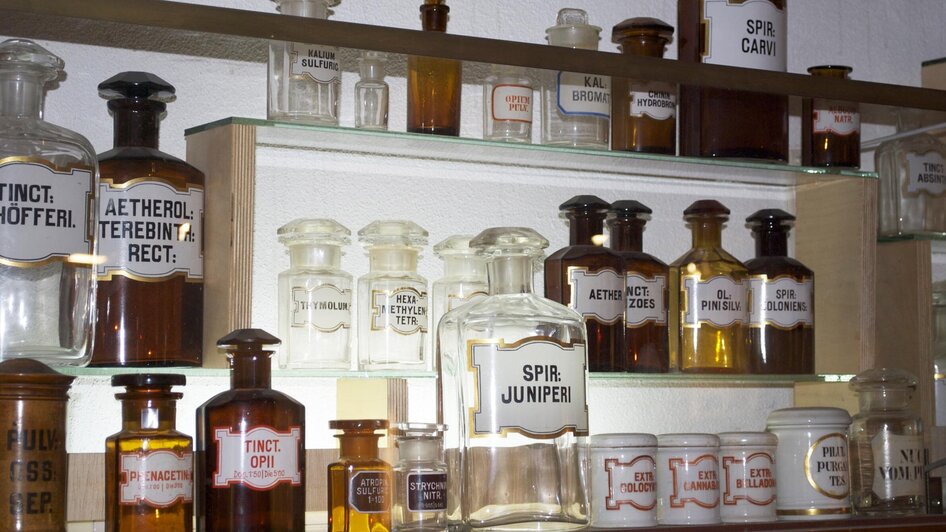 Regal mit alten Apothekerflaschen und Beschriftungen.