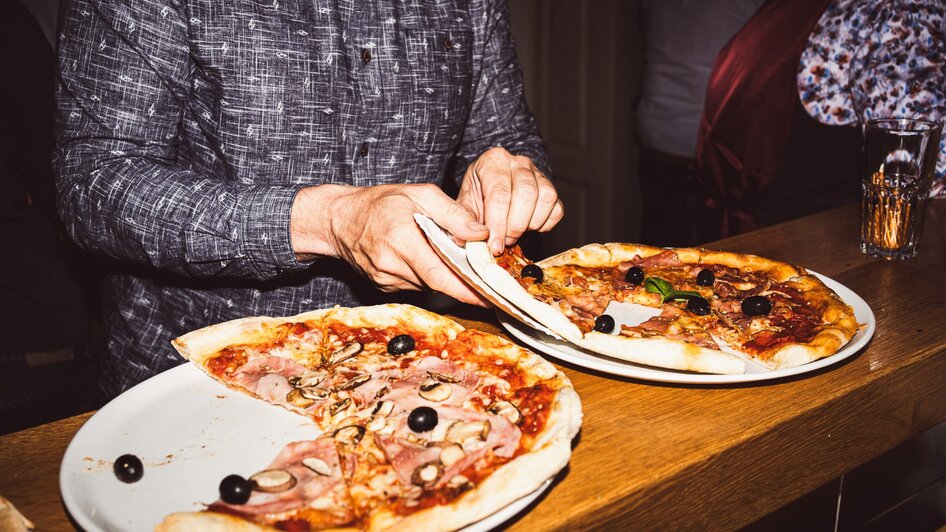Eine Person schneidet Pizza in einem Restaurant; zwei Pizzen auf Tellern.