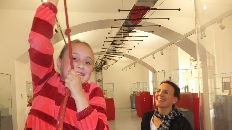 Ein Mädchen spielt in einem Museum, während eine Frau lächelt. | © UniGraz@Museum