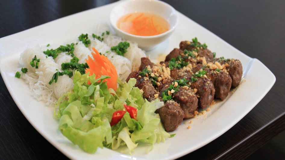 Leckeres Gericht mit gegrilltem Fleisch, Reisnudeln und Salat.