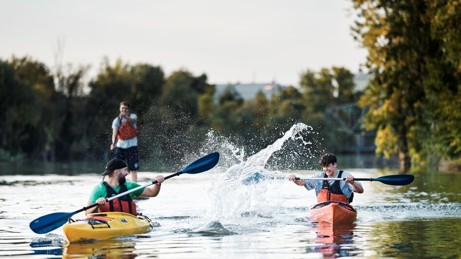 Boot-Verleih am Stadtstrand in Graz | © Stadtstrand Graz - Stefan Leitner Zwei Kajakfahrer paddeln auf ruhigem Wasser, während ein Dritter auf einem SUP steht und zuschaut. | © Stadtstrand Graz - Stefan Leitner