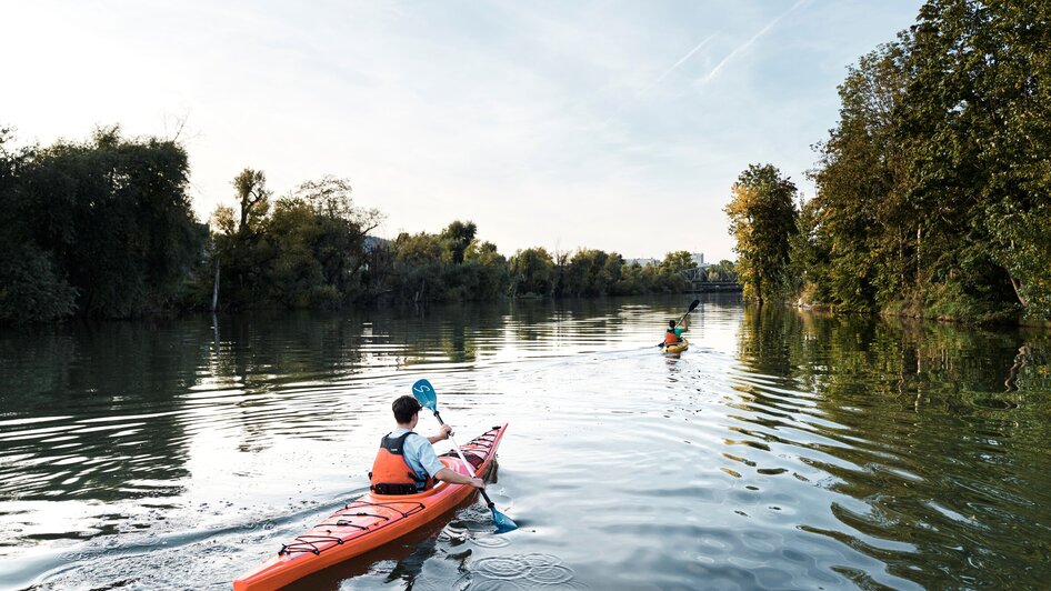 Boot-Verleih am Stadtstrand in Graz | © Stadtstrand Graz - Stefan Leitner Zwei Personen im Kajak paddeln auf der ruhigen Mur umgeben von Bäumen. | © Stadtstrand Graz - Stefan Leitner