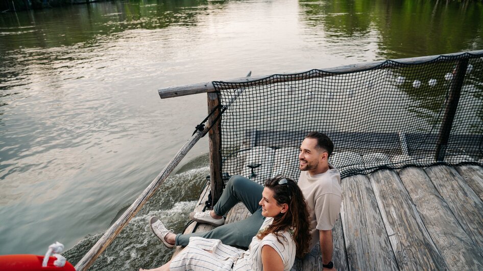 Floßfahren in Graz mit der Flößerei | © Graz Tourismus - Mias Photoart Paar sitzt am Fluss und genießt die Aussicht beim Floßfahren. | © Graz Tourismus - Mias Photoart