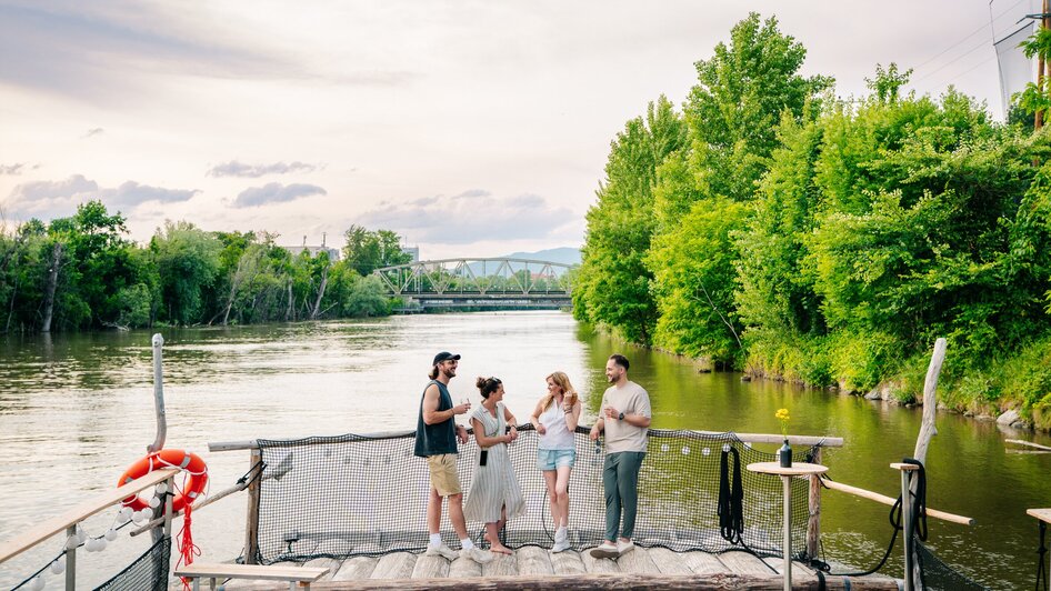 Floßfahren in Graz mit der Flößerei | © Graz Tourismus - Mias Photoart Gruppe von Freunden genießt Zeit am Fluss in Graz, umgeben von Bäumen. | © Graz Tourismus - Mias Photoart