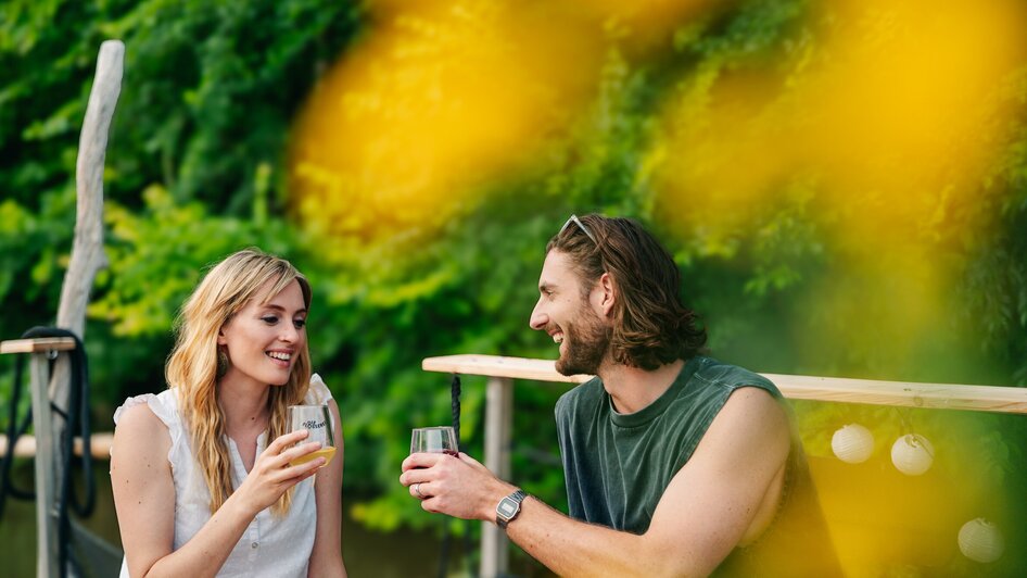 Floßfahren in Graz mit der Flößerei | © Graz Tourismus - Mias Photoart Ein Paar genießt Cocktails in entspannter Atmosphäre beim Floßfahren auf der Mur in Graz. | © Graz Tourismus - Mias Photoart