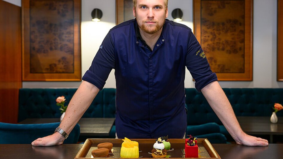 Küchenchef steht vor einem Tisch mit einer Platte mit verschiedenen Desserts in Graz.