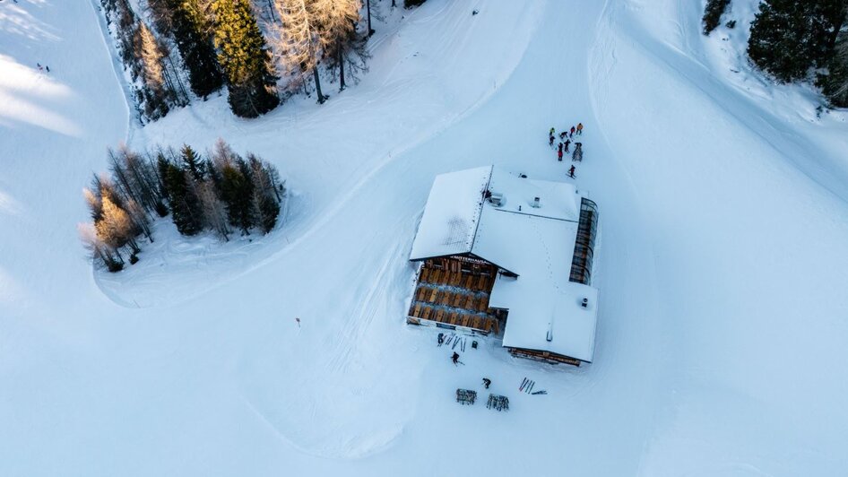 Holzhütte im Schnee mit Terrasse und abgestellten Skiern davor, umgeben von Bäumen. | © Mitterhausalm | Alpine Genusswelten