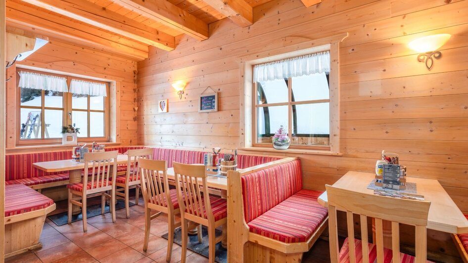 Gemütlicher Gastraum mit Holzwänden, roten Polsterbänken und Holztischen, warm beleuchtet. | © Mitterhausalm | Alpine Genusswelten