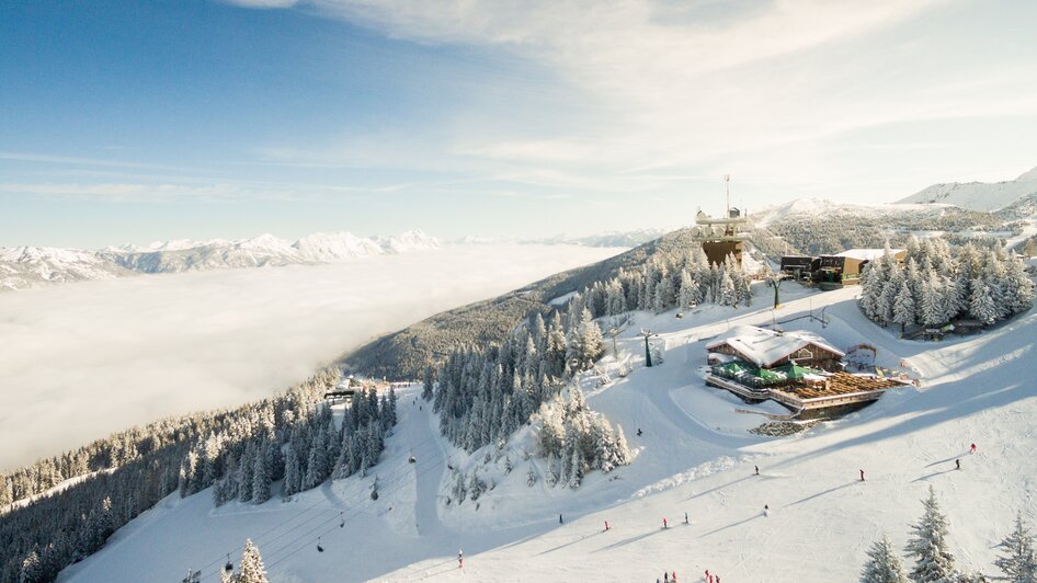 Die Schafalm in einer Winterlandschaft umgeben von Skifahrern, Schnee und Bäumen